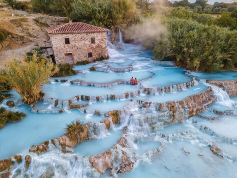 Le Cascate del Mulino di Saturnia viste dall'alto: le vasche naturali di travertino bianco digradano a terrazze con l'acqua termale turchese, accanto all'antico mulino in pietra circondato dai canneti.